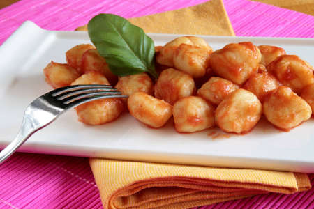 Plate of tomato sauce gnocchi on yellow napkin and pink place matの写真素材