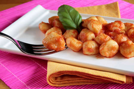 Closeup of potato gnocchi on a fork with a dish of tomato sauce gnocchi in the backgroundの写真素材