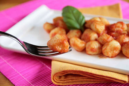 Closeup of potato gnocchi on a fork with a blurred dish of tomato sauce gnocchi in the backgroundの写真素材
