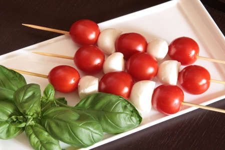 Vegetarian kebab of cherry tomatoes and mozzarella on skewers in a white dish, black backgroundの写真素材