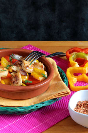 Delicious chicken with red and yellow peppers in a rustic bowl with a fork above itの写真素材