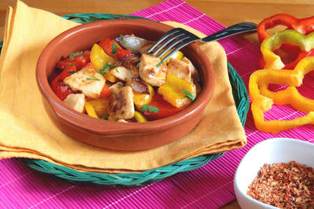 Delicious chicken with red and yellow peppers in a rustic bowl with a fork above itの写真素材