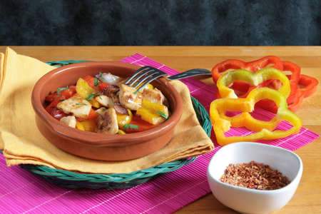 Delicious chicken with red and yellow peppers in a rustic bowl with a fork above itの写真素材