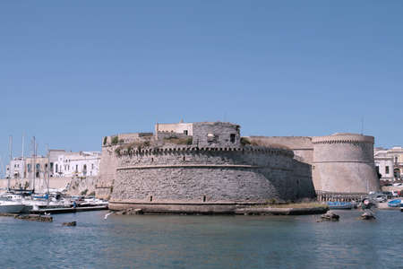 View of the Angevin castle in Gallipoli, Salento region (Apulia), with some boats in the harbor and the old town in backgroundの写真素材