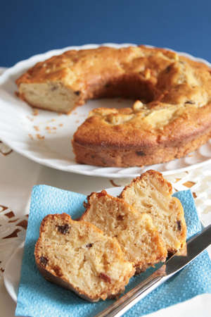 Slices of apple and raisins cake in a small plate with the whole cake slightly blurried in the backgroundの写真素材