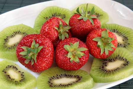 Closeup of kiwi and strawberries on a white dishの写真素材