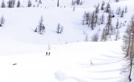 in the snow of the mountains in the Alps, two hikers climb towards the peaksの写真素材