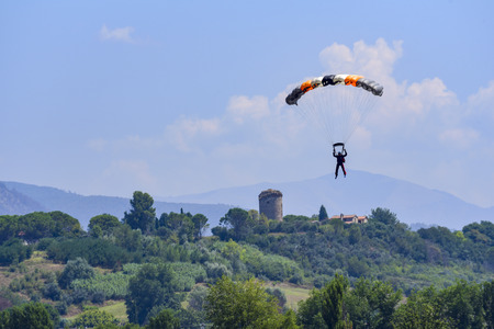 parachutist prepares for landing. On background the blue sky, mountains and green hills