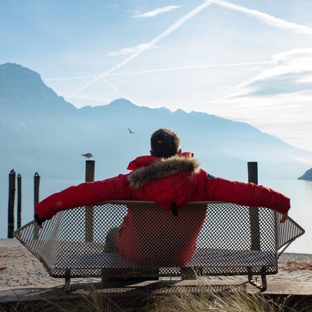 Man relaxing on a bench admires the view of Lake Garda
