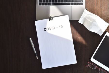 covid-19. Top view of desk with computer and white sheet for writingの写真素材