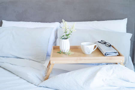 Breakfast in bed stationery mockup scene. Cup of coffee, newspaper and glasses on tray. White vase with small flowers. Valentine's day breakfast, lifestyle concept.の写真素材