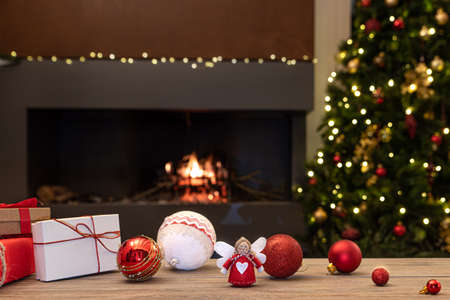 Cozy Christmas atmosphere with angel, decorations and gifts on wooden table in the foreground. In the background blurred the fireplace with fire, the Christmas tree and Christmas decorations. Selective focusの写真素材