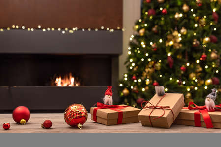Cozy Christmas atmosphere with Christmas gnomes and gifts on wooden table in the foreground. In the background blurred the fireplace with fire, the Christmas tree and Christmas decorations. Selective focusの写真素材