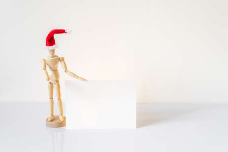 Christmas blank greeting card mock-up scene. Wooden mannequin posing on greeting card or gift list with red Santa Claus hat.の写真素材