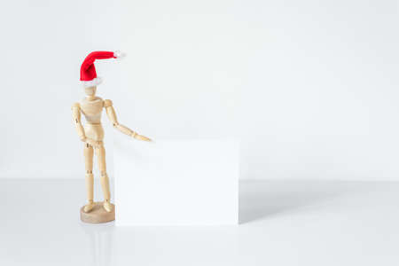Christmas blank greeting card mock-up scene. Wooden mannequin posing on greeting card or gift list with red Santa Claus hat.の写真素材