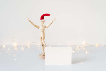 Christmas blank greeting card mock-up scene. Wooden mannequin posing on greeting card or gift list with red Santa Claus hat.の写真素材