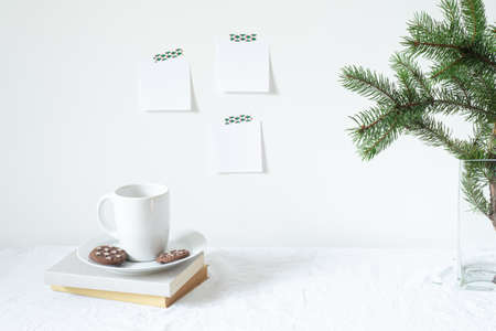 Festive breakfast still life.Cup of coffee with cookies, books and vase with fir branches.Empty notepads mockup hanging on the white wall.Christmas decor.Working space, home office.Happy new year resolutions, listの写真素材