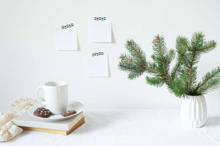 Festive breakfast still life.Cup of coffee with cookies, books and vase with fir branches.Empty notepads mockup hanging on the white wall.Christmas decor.Working space, home office.Happy new year resolutions, listの写真素材
