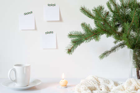 Festive breakfast still life.Cup of coffee, candle and vase with fir branches.Empty notepads mockup hanging on the white wall.Christmas decor.Working space, home office.Happy new year resolutions, listの写真素材