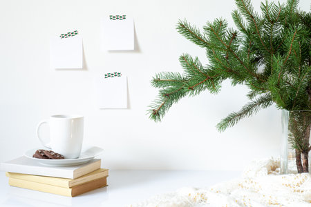 Festive breakfast still life.Cup of coffee with cookies, books and vase with fir branches.Empty notepads mockup hanging on the white wall.Christmas decor.Working space, home office.Happy new year resolutions, listの写真素材