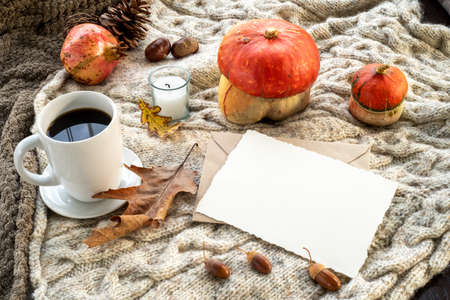Cozy autumn breakfast scene. Blank greeting card mockup and envelope with cup of coffee or tea, candle, pomegranate, pumpkins.Plaid wool background.Fall, thanksgiving day, halloween concept.の写真素材