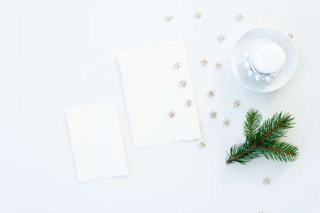 Christmas blank greeting card mockup scene. Festive winter wedding composition.Candle, fir tree branch, Christmas decoration on white table.Flat lay, top viewの写真素材