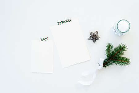 Christmas blank greeting card mockup scene. Festive winter wedding composition.Candle, fir tree branch, Christmas decoration on white table.Flat lay, top viewの写真素材