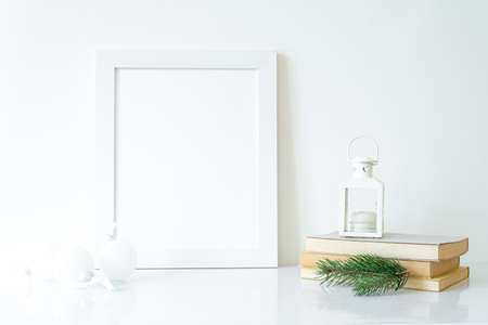 Vertical white blank frame mockup with Christmas lantern, books, fir tree branch and white Christmas decorations. Christmas, winter, festive concept. Copy spaceの写真素材