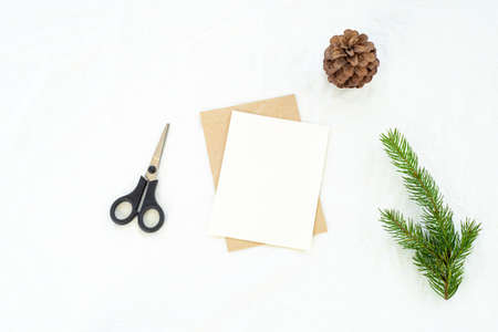 Christmas blank greeting card mock-up scene. Christmas decoration composition on white linen background with blank greeting card and envelope, fir branch, pine cone and scissors. Winter wedding composition.Top view, flat lay.の写真素材