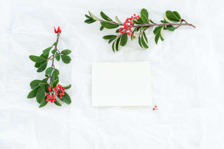 Festive greeting card, invitation card mockup. Christmas composition with branches of red berries, blank paper card on white crumpled paper background. Top view, flat layの写真素材