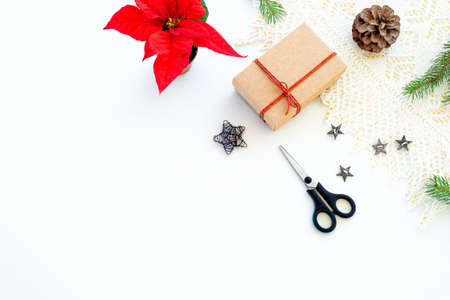 Composition of Christmas decorations on white background with gift box with red ribbon, pine branches, pine cone, decorative stars, scissor and red poinsettia. Greeting card mockup.Decorative corner.Background. Top view, flat layの写真素材