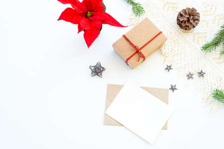 Composition of Christmas decorations on white background with gift box with red ribbon, pine branches, pine cone, decorative stars and red poinsettia. Blank greeting card, envelope mockup scene.Decorative corner.Background. Top view, flat layの写真素材