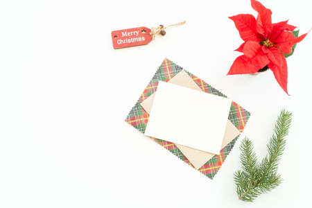 Christmas blank greeting card mock-up scene. Christmas decoration composition on white background with blank greeting card and envelope, fir branch, tag and red poinsettia. Top view, flat lay.Background.の写真素材