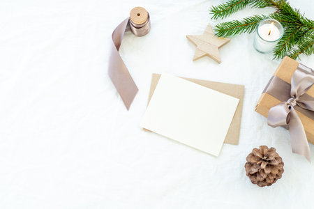 Christmas decorations composition. Decorative corner.Christmas blank greeting card mock-up scene. Gift christmas box with ribbon, fir branch, pine cone, wooden star and lighted candle. White linen background.Copy space, top view, flat layの写真素材