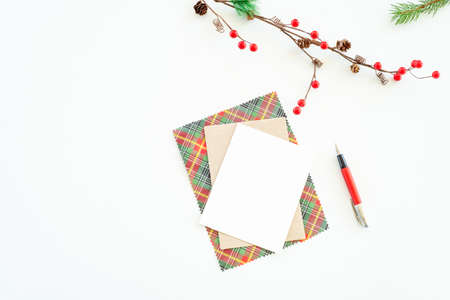 Christmas blank greeting card mock-up scene. Christmas decoration composition on white background with blank greeting card and envelope, fir branch, pen and decorative red berries. Top view, flat lay.Background.の写真素材