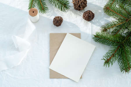 Blank greeting card, invitation card mockup.Christmas decoration scene with card and envelope, ribbon, fir branches and wooden balls.White linen background.Top view, flat lay.Winter wedding conceptの写真素材