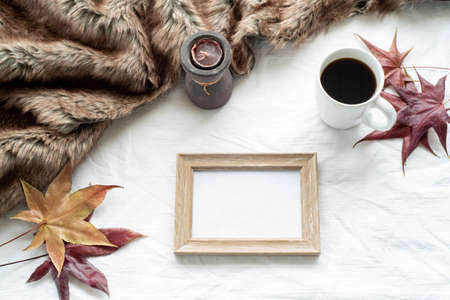 Autumn breakfast scene. Blank wooden picture frame mock-up with maple leaves, cup of coffee, scented candle and plaid. White tablecloth background. Top view, flat layの写真素材