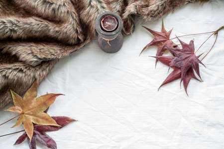 Autumn greeting card mockup scene with maple leaves, scented candle and plaid. White tablecloth background.Top view, flat lay, copy spaceの写真素材