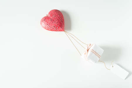 Christmas present hanging on a big red heart.Hot air balloon carrying the gift box in flight with hanging a blank label.Valentine's day holiday concept Copy space, top view, flat layの写真素材