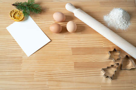 Homemade Christmas cookies. Blank greeting card or business card on wooden work table. Rolling pin, cookie cutters, eggs. Template for recipes.Top view, flat layの写真素材