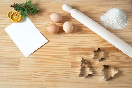 Homemade Christmas cookies. Blank greeting card or business card on wooden work table. Rolling pin, cookie cutters, eggs. Template for recipes.Top view, flat layの写真素材