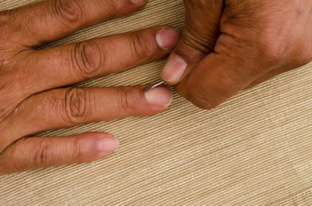 a multiracial man uses a cuticle pusher to give himself a manicure on the ring finger.. Concept of...