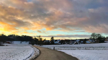 Winter landscape with snow covered fields and village in the background at sunset
