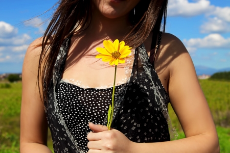 Detail of the chest of a girl holding a yellow flower in a spring dayの写真素材