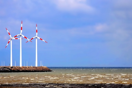Red and white windmills towers over a landscape of seaの写真素材