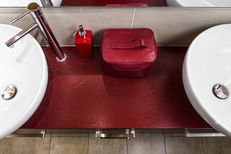 sinks with a circular shape from above, installated on a red wooden surface surround a soap dispenser and a red leather beauty caseの写真素材