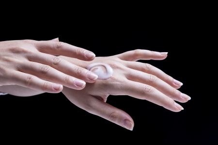 Female hands, isolated on black background, are smearing cream on themselvesの写真素材