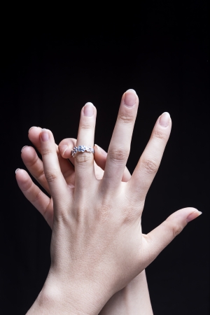 Female hands, isolated on a black background, are wearing an engagement ringの写真素材