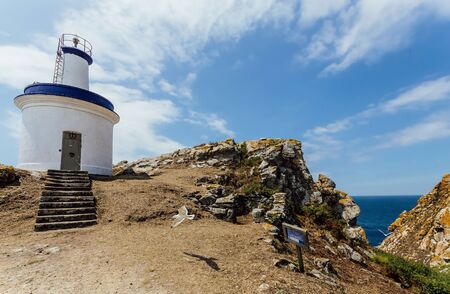 White and blue lighthouse on a cliff, surronded by clouds