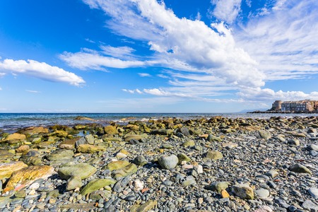 Perspective from a stones beach of a bay with a village on its pier and stormy clouds in the skyの写真素材
